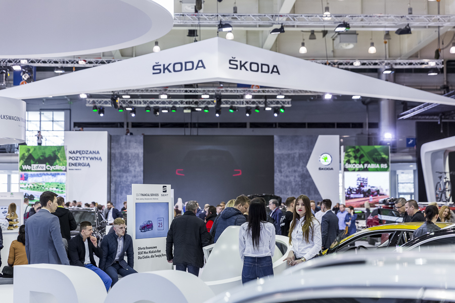 Realizacja zabudowy dla wiodących marek motoryzacyjnych podczas Poznań Motor Show to monumentalny projekt o łącznej powierzchni przekraczającej 4500 m². Jako BWS EXPO zapewniliśmy kompleksowe wsparcie techniczne i wykonawcze, tworząc spójne, a jednocześnie unikalne przestrzenie ekspozycyjne dla marek takich jak BMW, Porsche, Audi, Rolls-Royce oraz całej grupy Volkswagen (Skoda, Seat, VW). Kluczowe aspekty techniczno-wykonawcze: Skala i Logistyka: Równoczesna budowa stoisk dla wielu marek premium wymagała perfekcyjnej koordynacji prac montażowych oraz logistyki materiałowej w kilku halach targowych. Design i Materiały: Każda przestrzeń została wykończona zgodnie z rygorystycznymi standardami wizualnymi (Corporate Identity) poszczególnych brandów. Wykorzystano m.in. eleganckie okładziny drewniane dla stref luksusowych (Rolls-Royce, Porsche), nowoczesne konstrukcje loftowe oraz wysokiej jakości posadzki targowe. Systemy Podwieszeń i Multimeadia: Zastosowano zaawansowane konstrukcje kratownicowe z wielkoformatowymi ekranami LED, dynamicznym oświetleniem scenicznym oraz potężnymi elementami brandingowymi (np. charakterystyczne ringi Volkswagen Financial Services czy kubiki BMW), które zapewniały widoczność marek z dużej odległości. Strefy Specjalne: Realizacja objęła budowę dwupoziomowych stref VIP, butików Lifestyle Shop (BMW), profesjonalnych recepcji z grafikami oraz interaktywnych stoisk usług finansowych. Dzięki doświadczeniu w obsłudze największych wydarzeń motoryzacyjnych, dostarczyliśmy infrastrukturę, która połączyła technologiczną nowoczesność z prestiżem, tworząc idealne tło dla premier motoryzacyjnych najwyższej klasy.