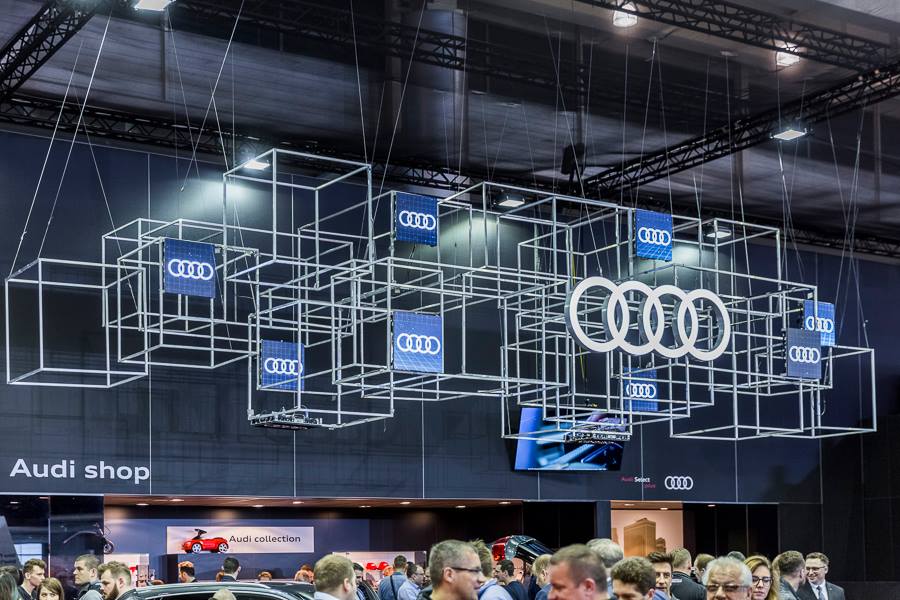 Realizacja zabudowy dla wiodących marek motoryzacyjnych podczas Poznań Motor Show to monumentalny projekt o łącznej powierzchni przekraczającej 4500 m². Jako BWS EXPO zapewniliśmy kompleksowe wsparcie techniczne i wykonawcze, tworząc spójne, a jednocześnie unikalne przestrzenie ekspozycyjne dla marek takich jak BMW, Porsche, Audi, Rolls-Royce oraz całej grupy Volkswagen (Skoda, Seat, VW). Kluczowe aspekty techniczno-wykonawcze: Skala i Logistyka: Równoczesna budowa stoisk dla wielu marek premium wymagała perfekcyjnej koordynacji prac montażowych oraz logistyki materiałowej w kilku halach targowych. Design i Materiały: Każda przestrzeń została wykończona zgodnie z rygorystycznymi standardami wizualnymi (Corporate Identity) poszczególnych brandów. Wykorzystano m.in. eleganckie okładziny drewniane dla stref luksusowych (Rolls-Royce, Porsche), nowoczesne konstrukcje loftowe oraz wysokiej jakości posadzki targowe. Systemy Podwieszeń i Multimeadia: Zastosowano zaawansowane konstrukcje kratownicowe z wielkoformatowymi ekranami LED, dynamicznym oświetleniem scenicznym oraz potężnymi elementami brandingowymi (np. charakterystyczne ringi Volkswagen Financial Services czy kubiki BMW), które zapewniały widoczność marek z dużej odległości. Strefy Specjalne: Realizacja objęła budowę dwupoziomowych stref VIP, butików Lifestyle Shop (BMW), profesjonalnych recepcji z grafikami oraz interaktywnych stoisk usług finansowych. Dzięki doświadczeniu w obsłudze największych wydarzeń motoryzacyjnych, dostarczyliśmy infrastrukturę, która połączyła technologiczną nowoczesność z prestiżem, tworząc idealne tło dla premier motoryzacyjnych najwyższej klasy.