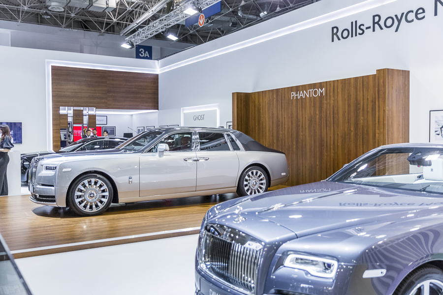Realizacja zabudowy dla wiodących marek motoryzacyjnych podczas Poznań Motor Show to monumentalny projekt o łącznej powierzchni przekraczającej 4500 m². Jako BWS EXPO zapewniliśmy kompleksowe wsparcie techniczne i wykonawcze, tworząc spójne, a jednocześnie unikalne przestrzenie ekspozycyjne dla marek takich jak BMW, Porsche, Audi, Rolls-Royce oraz całej grupy Volkswagen (Skoda, Seat, VW). Kluczowe aspekty techniczno-wykonawcze: Skala i Logistyka: Równoczesna budowa stoisk dla wielu marek premium wymagała perfekcyjnej koordynacji prac montażowych oraz logistyki materiałowej w kilku halach targowych. Design i Materiały: Każda przestrzeń została wykończona zgodnie z rygorystycznymi standardami wizualnymi (Corporate Identity) poszczególnych brandów. Wykorzystano m.in. eleganckie okładziny drewniane dla stref luksusowych (Rolls-Royce, Porsche), nowoczesne konstrukcje loftowe oraz wysokiej jakości posadzki targowe. Systemy Podwieszeń i Multimeadia: Zastosowano zaawansowane konstrukcje kratownicowe z wielkoformatowymi ekranami LED, dynamicznym oświetleniem scenicznym oraz potężnymi elementami brandingowymi (np. charakterystyczne ringi Volkswagen Financial Services czy kubiki BMW), które zapewniały widoczność marek z dużej odległości. Strefy Specjalne: Realizacja objęła budowę dwupoziomowych stref VIP, butików Lifestyle Shop (BMW), profesjonalnych recepcji z grafikami oraz interaktywnych stoisk usług finansowych. Dzięki doświadczeniu w obsłudze największych wydarzeń motoryzacyjnych, dostarczyliśmy infrastrukturę, która połączyła technologiczną nowoczesność z prestiżem, tworząc idealne tło dla premier motoryzacyjnych najwyższej klasy.