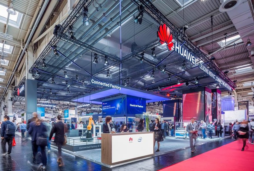Realizacja dla marki Huawei na targach Hannover Messe 2018 to imponujące stoisko o powierzchni 600 m², które stanowi kwintesencję nowoczesnych technologii i zaawansowanej architektury targowej. Projekt bazuje na otwartej przestrzeni, zdominowanej przez wielkogabarytowe konstrukcje podwieszane i zintegrowane systemy multimedialne, co idealnie wpisuje się w technologiczną tożsamość brandu. Charakterystycznym elementem stoiska jest rozbudowana konstrukcja kratownicowa, na której osadzono potężne logotypy Huawei oraz zaawansowane systemy oświetlenia scenicznego, zapewniające doskonałą widoczność ekspozycji w całej hali. Całość stoiska została podzielona na tematyczne sekcje, w tym strefy prezentacji robotyki przemysłowej oraz wydzielone przestrzenie do rozmów biznesowych o wysokim standardzie wykończenia. Jako BWS EXPO zrealizowaliśmy tę kompleksową zabudowę, dbając o perfekcyjne wykończenie.
