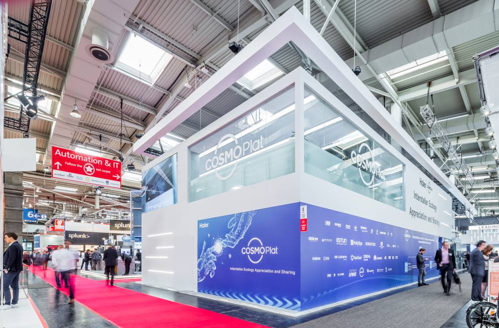Realizacja stoiska marki Haier na targach Hannover Messe 2019 to zaawansowana technicznie, piętrowa konstrukcja o łącznej powierzchni 510 m². Wykonanie oparto na solidnym systemie stalowym, który pozwolił na stworzenie przestronnej antresoli z przeszklonymi balustradami, pełniącą funkcję strefy biznesowej. Parter został zaprojektowany jako otwarta przestrzeń ekspozycyjna, zdominowana przez wielkogabarytowe ekrany LED oraz interaktywne panele prezentujące rozwiązania z zakresu przemysłowego internetu rzeczy. Całość zabudowy wykończono w minimalistycznej bieli, którą przełamują dynamiczne elementy multimedialne oraz rozbudowany system podświetleń liniowych zintegrowanych z architekturą stoiska. Istotnym elementem montażowym było precyzyjne osadzenie konstrukcji podwieszanych, w tym efektownych, świecących logotypów oraz transparentnych tablic informacyjnych.